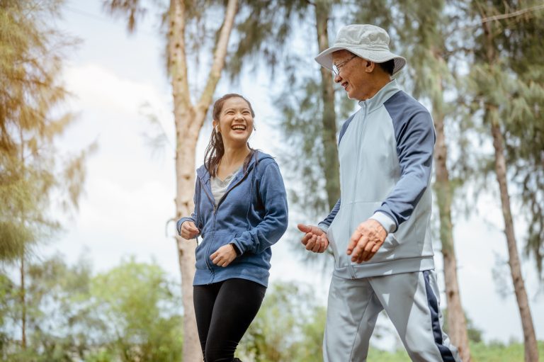 A woman and grandfather are walking jogging on the street at the park. Grandfather talk about the story of  past life experiences. Healthy and lifestyle concept.