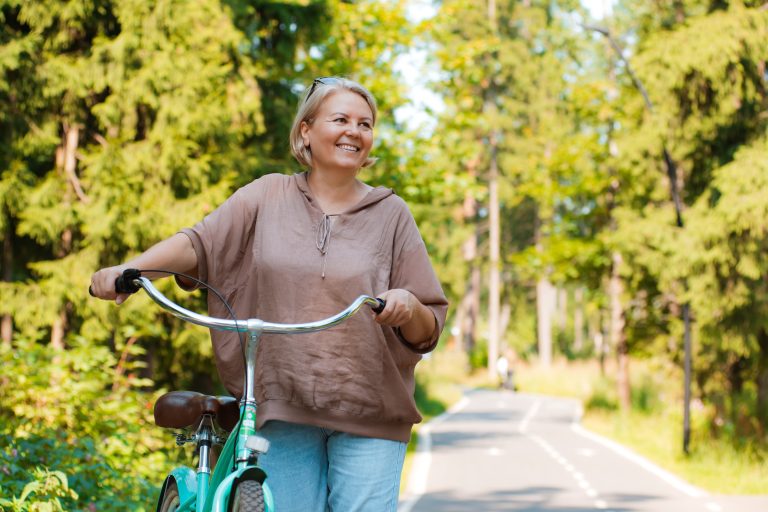 Senior older elderly modern woman rides a bicycle in a city park in the forest. Active pensioner, health lifestyle